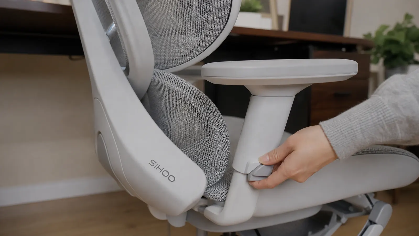 Close-up of a hand adjusting the armrest height on a mesh ergonomic office chair