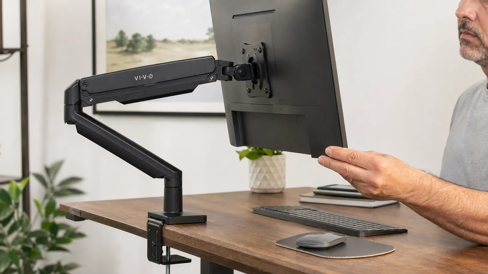 Close-up of a hand adjusting the tilt and height of a monitor mounted on a gas-spring articulating arm