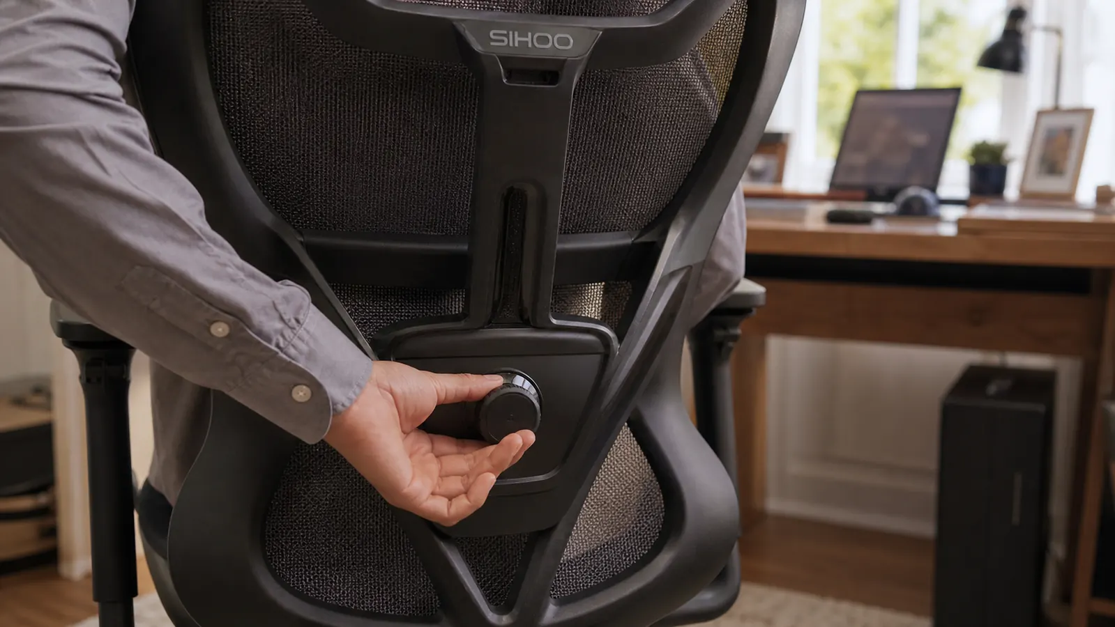 Close-up of a hand turning the lumbar support adjustment dial on the back of a mesh ergonomic office chair.