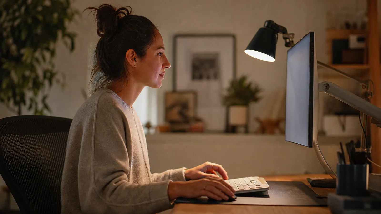 Home office desk setup viewed from the side showing a key light positioned at eye level next to a monitor