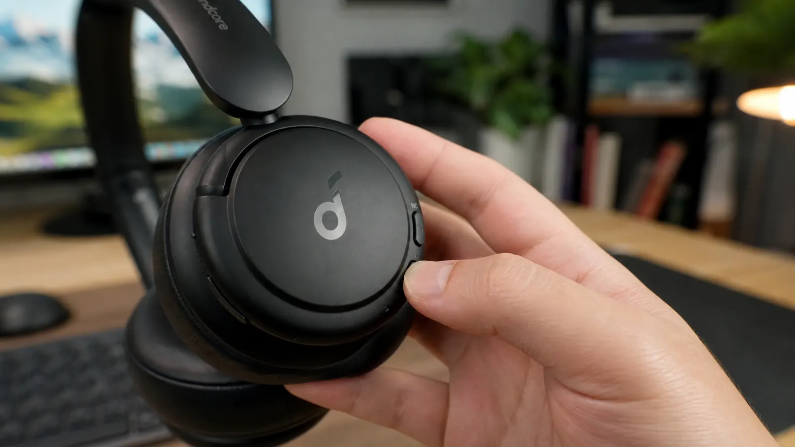 Close-up of a hand pressing the noise cancelling mode button on the ear cup of a black over-ear headphone
