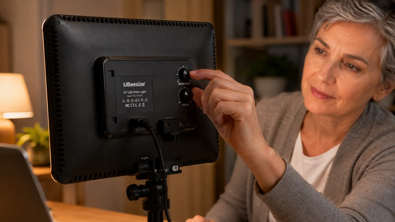 Close-up of a hand adjusting the brightness dial on the back of a rectangular key light mounted on an articulating desk arm