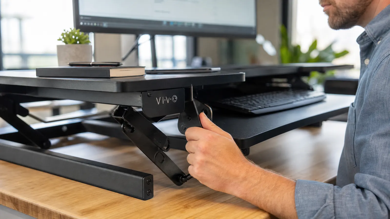 Close-up of a hand squeezing the height-adjustment handle on the side of a black standing desk converter