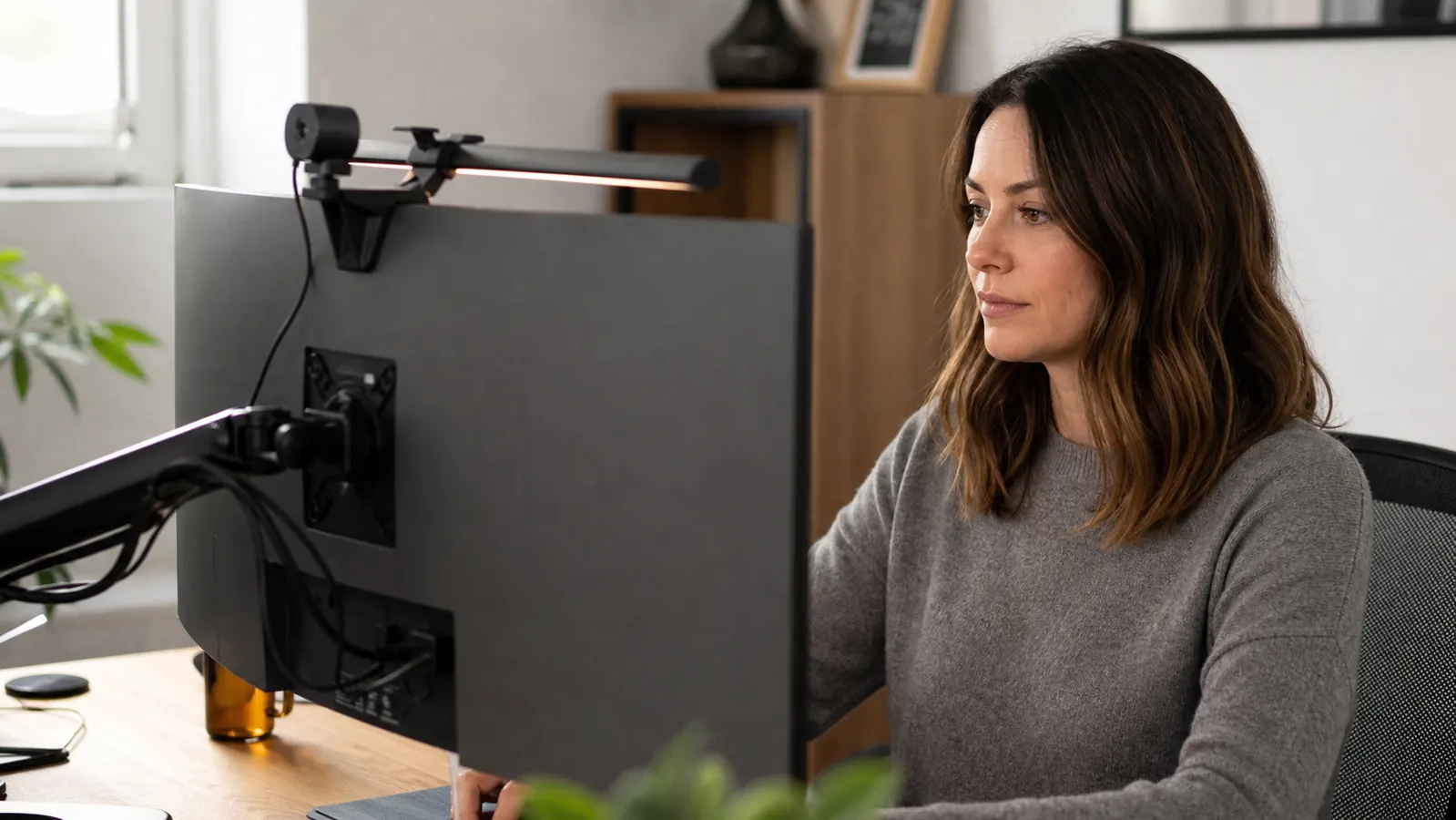 Desk setup with a curved monitor on an articulating arm, a small clamp-on light bar mounted above the screen, and a webcam clipped to the top edge